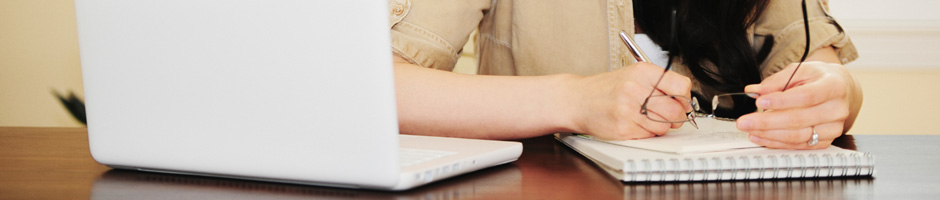 Woman taking notes on a pad of paper while looking at a computer screen